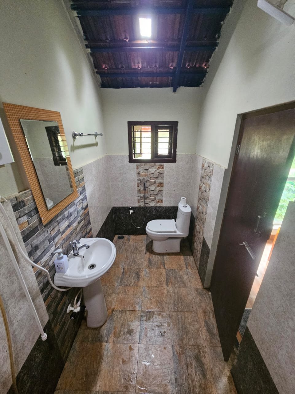 Tiled bathroom with pedestal wash basin, mirror, western toilet and hand shower