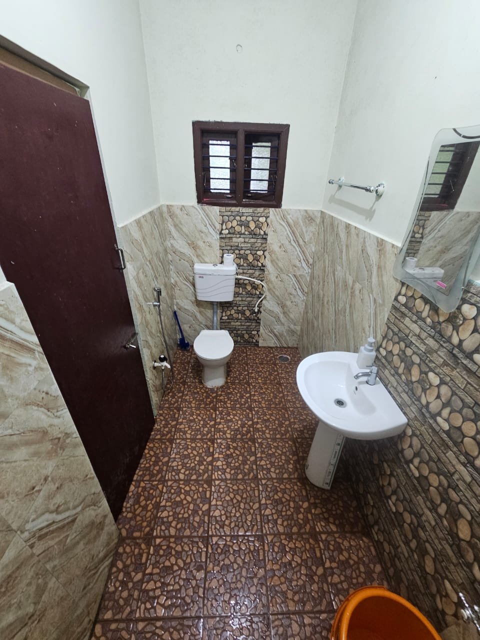Second bathroom with stone-finish tiles, wash basin, mirror and western toilet