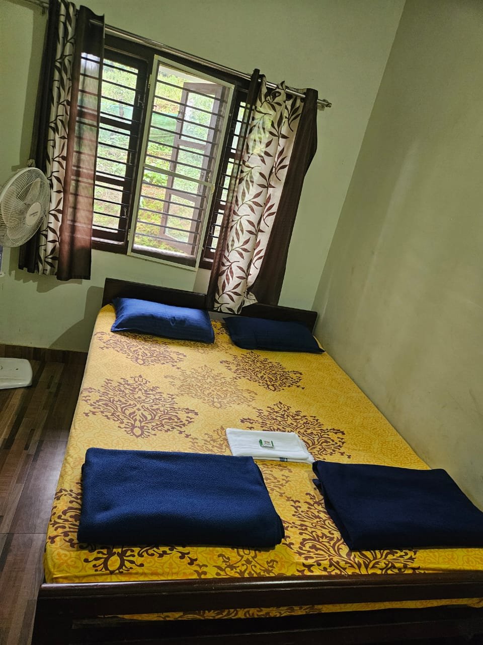 Double room with yellow bedding, blue pillows, fan and a window opening to the garden